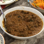 Lamb curry in a white bowl with a metal spoon.